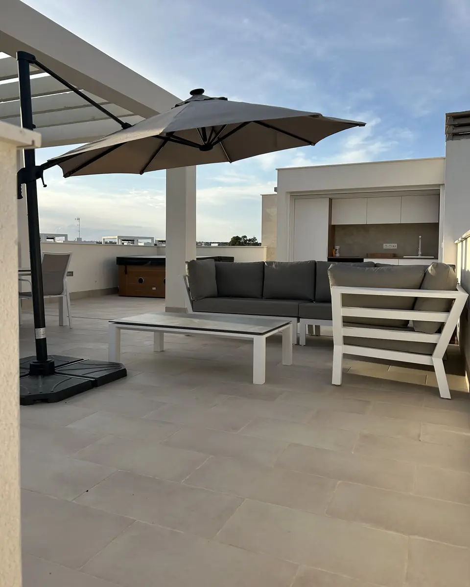 De loungebank met salontafel onder een grote parasol op het dakterras
